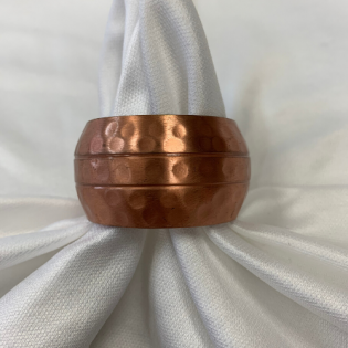 Copper hammered napkin ring holding a white cloth napkin on a light background