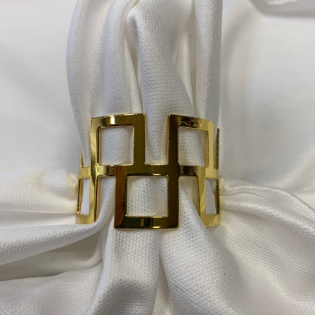Gold geometric bracelet with square cutouts on white fabric background