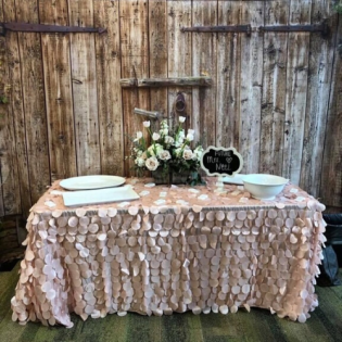 Rustic dessert table with blush floral decor, white plates, and a wooden backdrop at an outdoor event