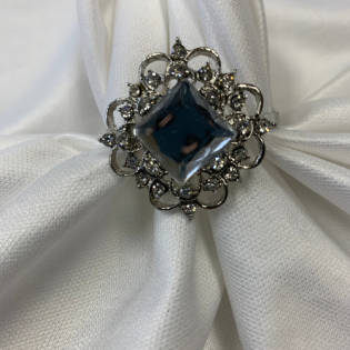 Silver floral brooch with a dark blue gemstone on white fabric