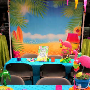 Tropical-themed party table with pink flamingos, colorful tableware, and a beach backdrop backdrop.