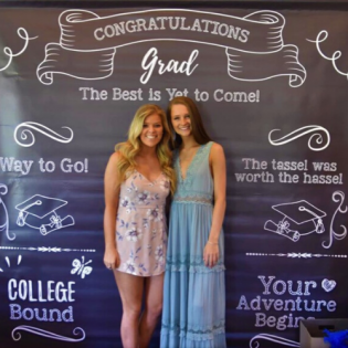 Two graduates posing in front of a chalkboard-style graduation backdrop with “Congratulations Grad” and “College Bound” text