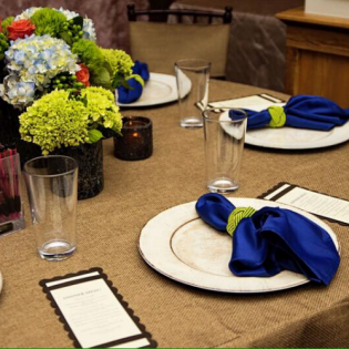 Set dining table with white plates, blue napkins, glassware, and yellow-green floral centerpieces