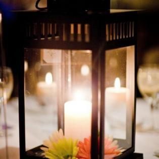 Black lantern with glowing white candles and small flowers on a table at a formal event