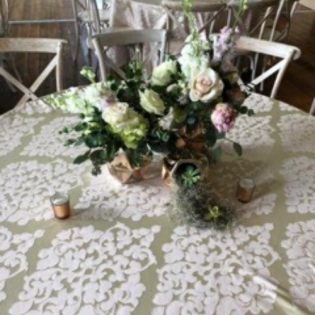 Floral centerpiece with white, pink, and green flowers on a lace-covered round table
