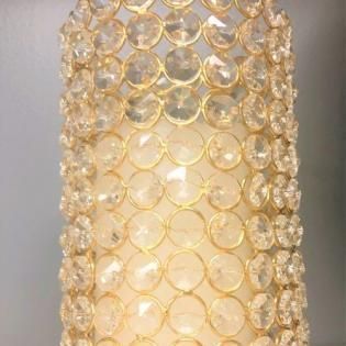 Gold crystal beaded cylindrical lampshade glowing warmly against a neutral wall