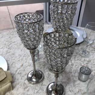 Three silver decorative goblets on a light rug beside a small glass candle holder