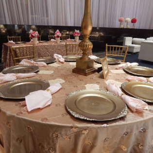 Round banquet table with gold chargers, pink napkins, and a gold centerpiece in a formal event hall
