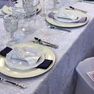 Elegant table setting with white plates, folded napkins, silverware, and glassware on a lavender tablecloth