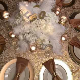 Elegant white floral centerpiece with feathers and gold accents on a set dining table.
