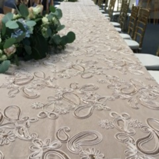 Lace table runner with green floral arrangement on a long banquet table with gold chairs