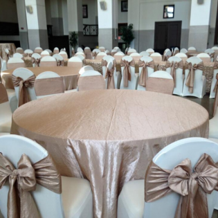 Elegant banquet hall with round tables, white chair covers, and gold satin bows on the chairs