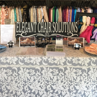 Event booth for “Elegant Chair Solutions” with displayed fabrics, accessories, and decorative table setup