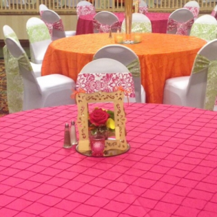 Decorated banquet tables with pink and orange covers, white chairs, and floral centerpieces in a hall
