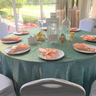 Round teal-decorated table set for a wedding reception with plates, napkins, lanterns, and glass centerpieces
