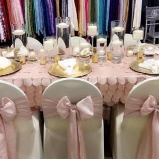 Pink-themed banquet table with gold chargers, white decor, and blush bow-covered chairs