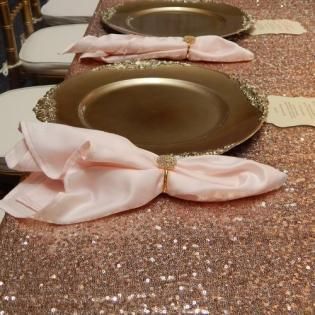 Gold plates on a glittery tablecloth, each topped with a pale pink satin bow napkin.