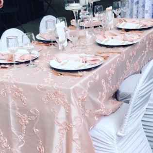 Set table with pink floral tablecloth, wine glasses, and white chair covers at a banquet event