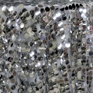 Close-up of silver sequins on shimmering fabric with a reflective, textured surface