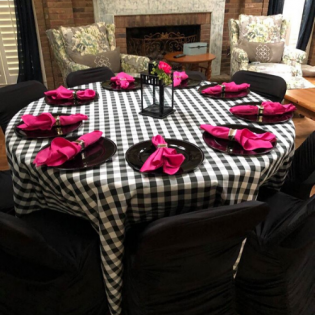 Round dining table with black-and-white checkered cloth, pink napkins, and black chairs in a living room