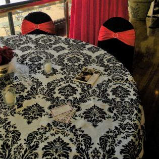 Dining table with black-and-white damask cloth, red chairs, candles, and scattered cards in a room