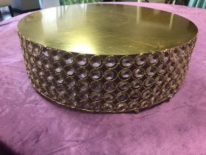 Gold round tabletop with a textured, studded metal base on a purple surface