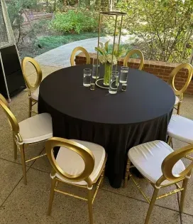 Gold chairs around a black round table with floral centerpieces in an outdoor patio setting
