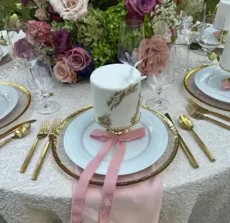 Elegant table setting with white plates, gold cutlery, pink ribbons, and floral centerpieces