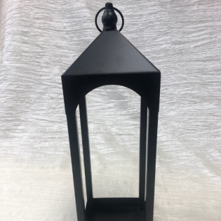 Black metal lantern with a peaked top and arched opening, hanging against a light fabric background