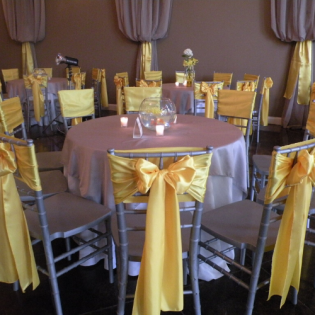 Round banquet table with pink cloth and yellow ribboned chairs in a decorated event room