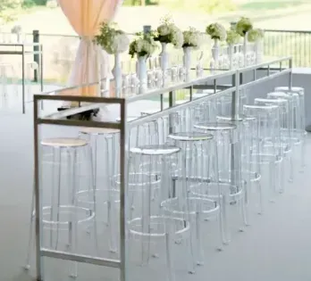 Modern white bar setup with clear stools and floral decor in a bright event venue
