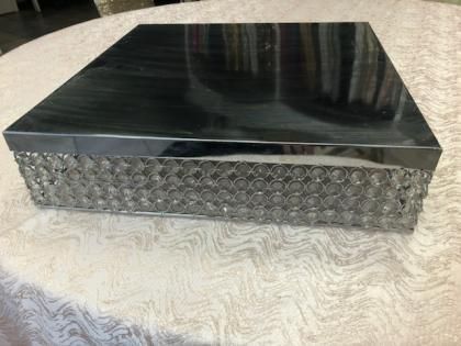 Black rectangular box with a glossy lid and textured silver side panel on a patterned tablecloth