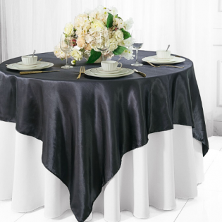 Round banquet table with white flowers, dark gray tablecloth, and white chair covers in a bright room