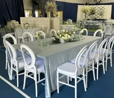 White banquet table with matching chairs and floral centerpieces in a decorated event hall