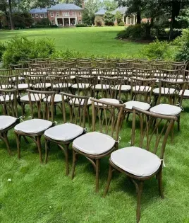 Rows of white-cushioned wooden chairs set on a green lawn for an outdoor ceremony, with a house in the background