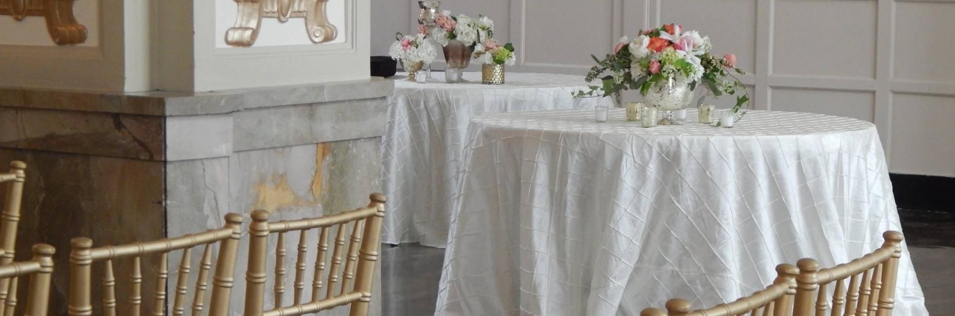 Round tables with white cloths and floral centerpieces set in a rustic dining room