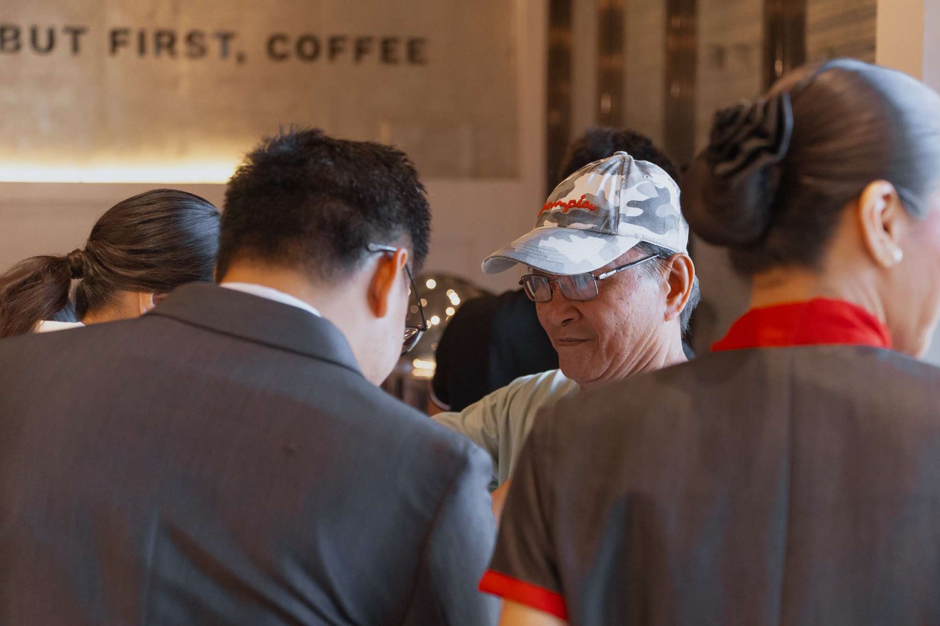 A group of people standing in front of a sign that says but first coffee