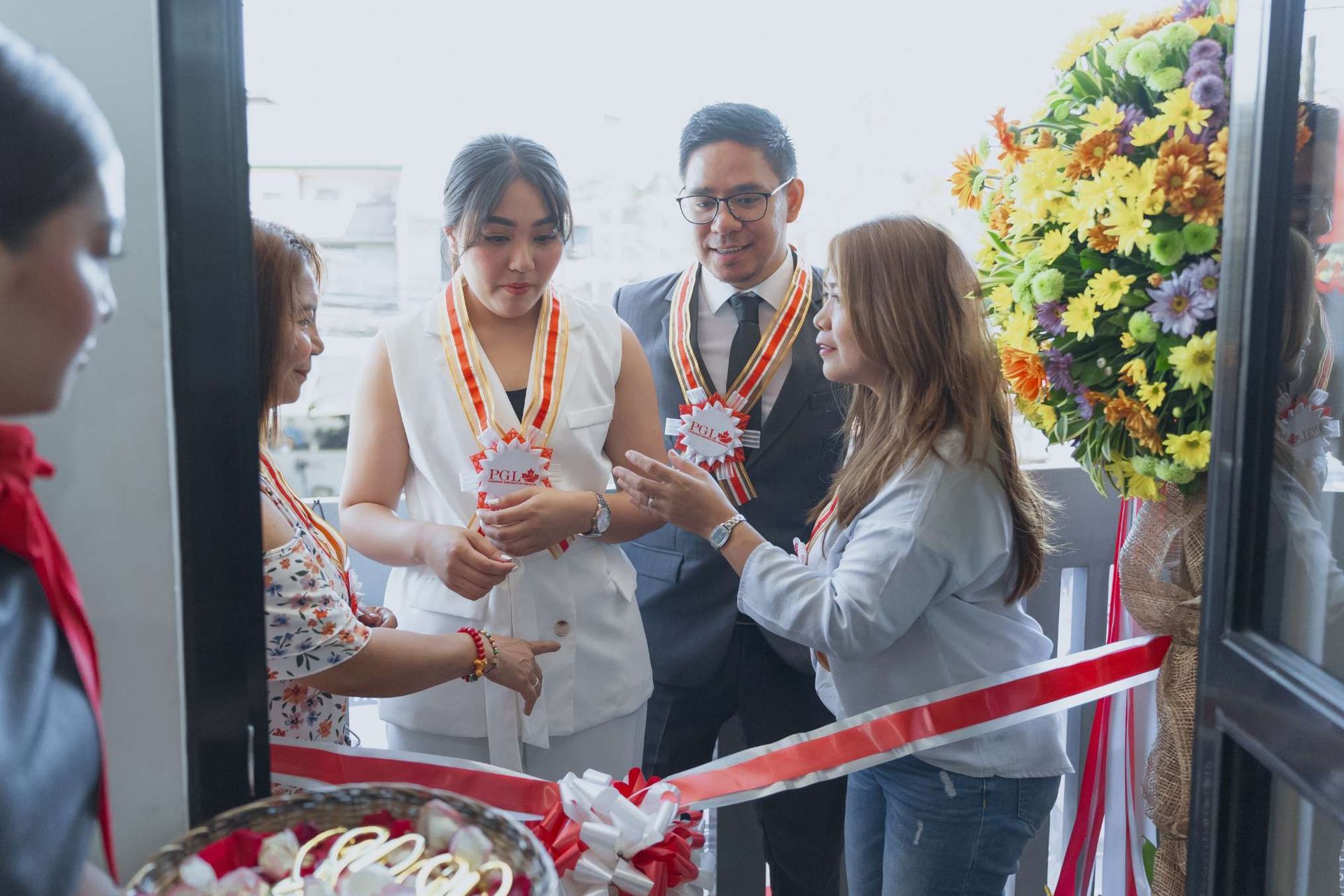 A group of people are cutting a red and white ribbon.