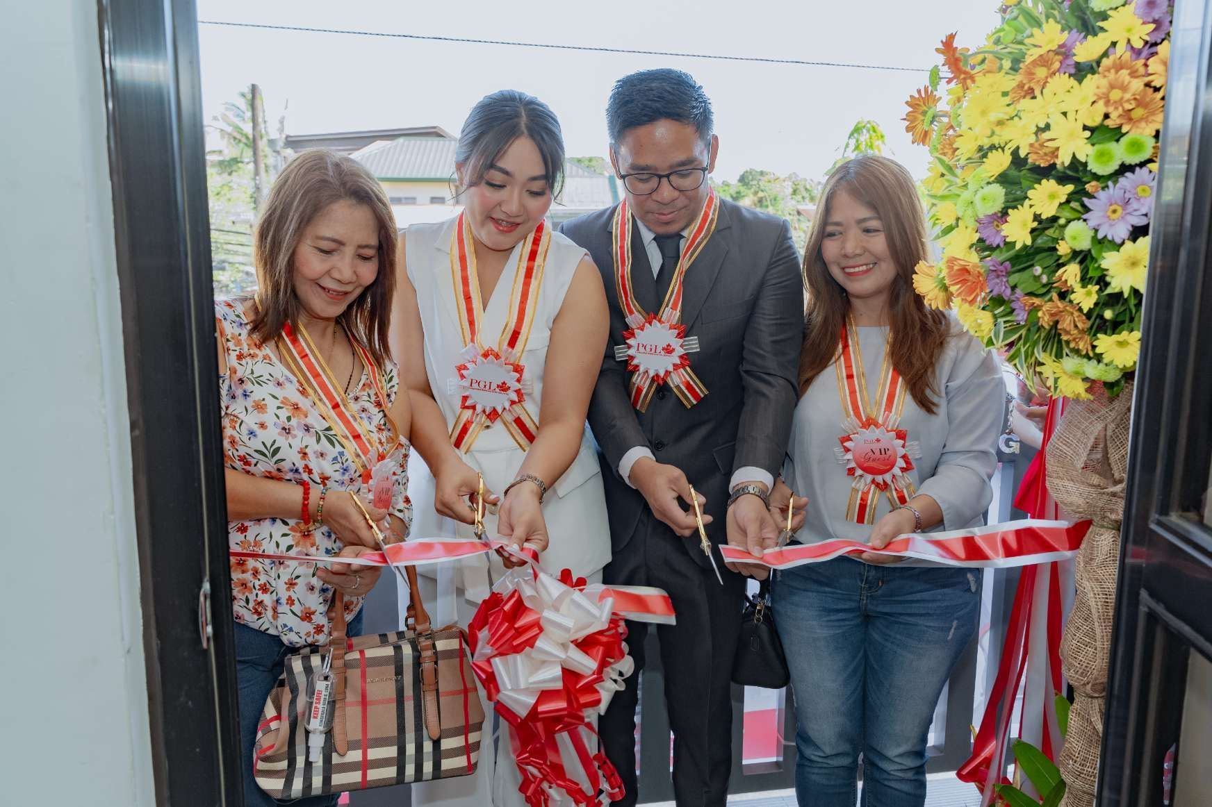 A group of people are cutting a red and white ribbon.