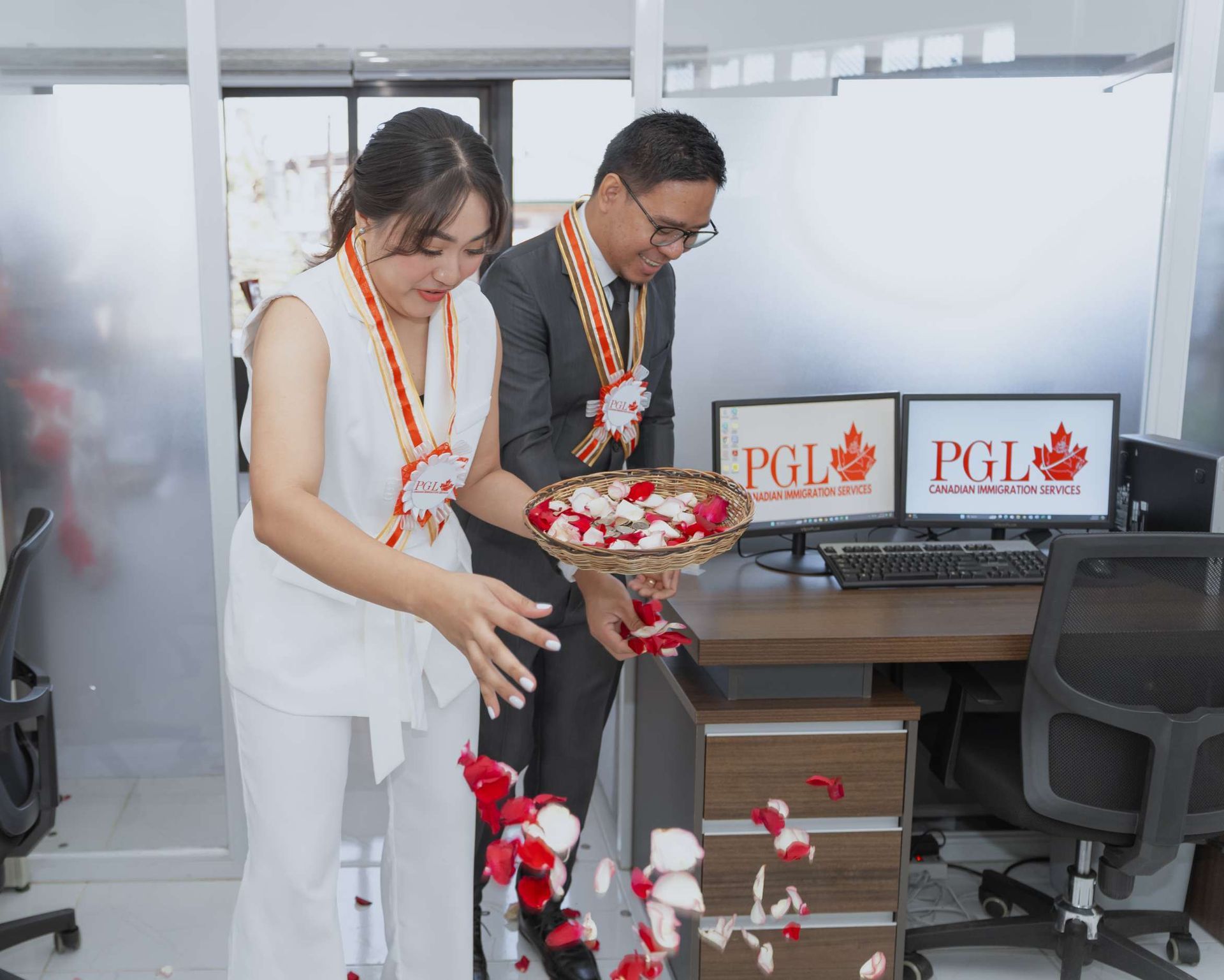 A man and a woman are standing in an office holding a basket of flowers.