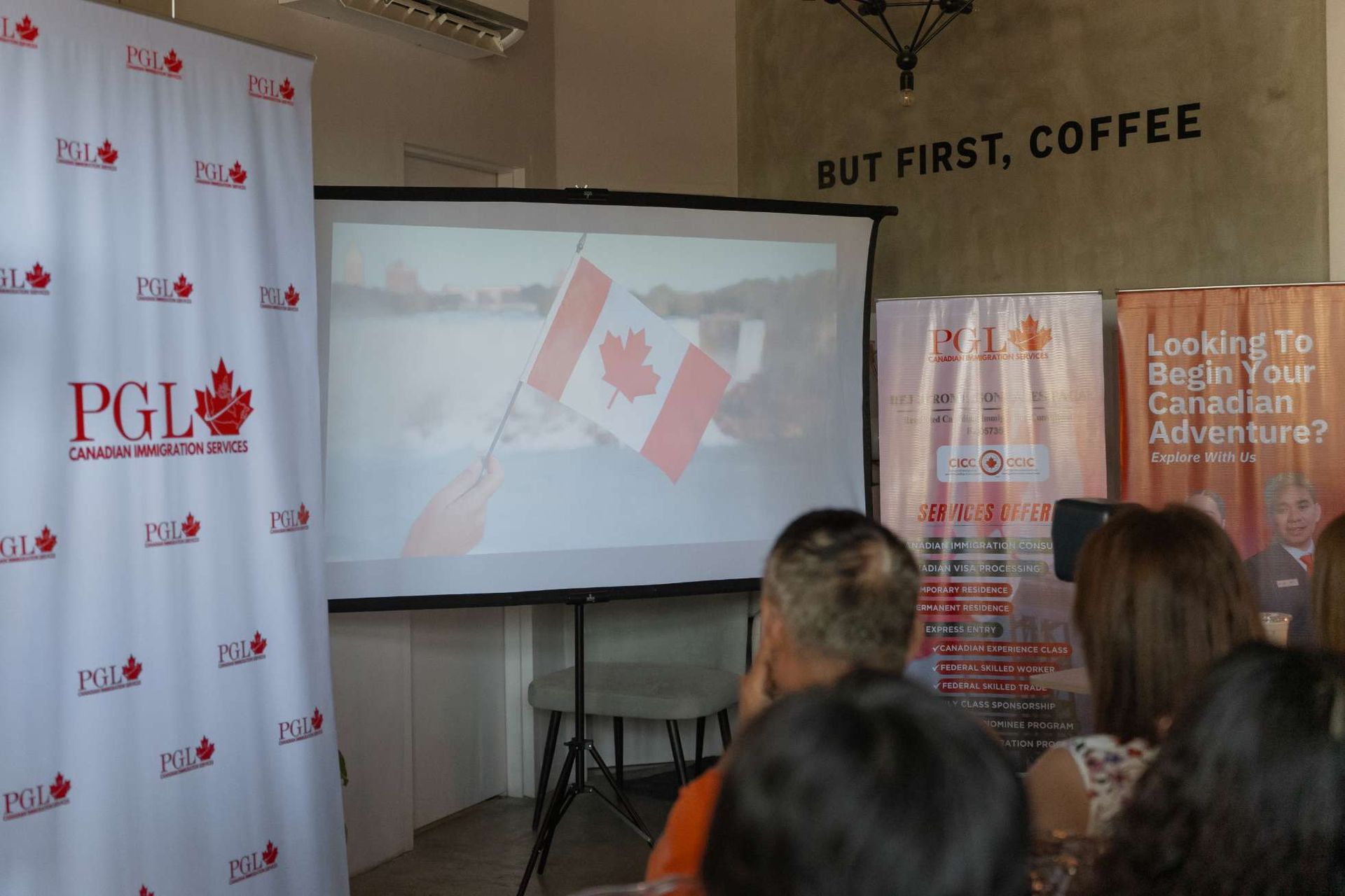 A group of people are sitting in front of a projector screen with a canadian flag on it.