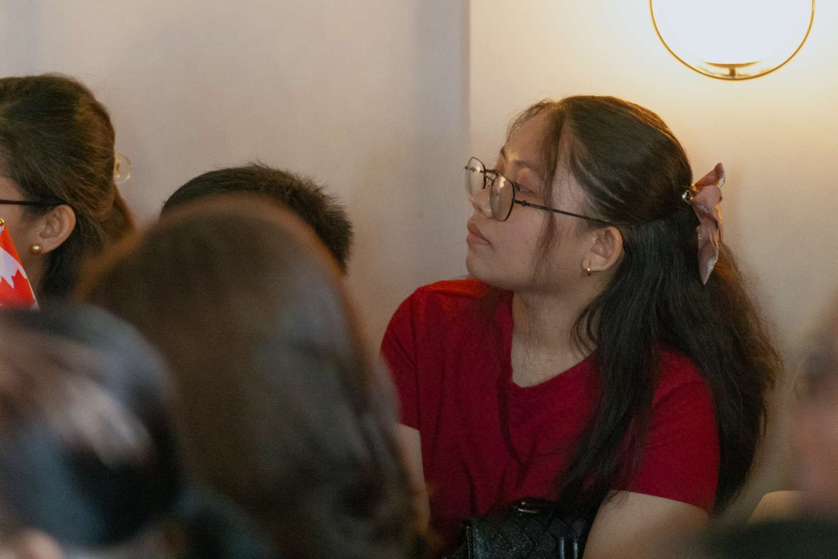 A woman wearing glasses is sitting in a crowd of people.