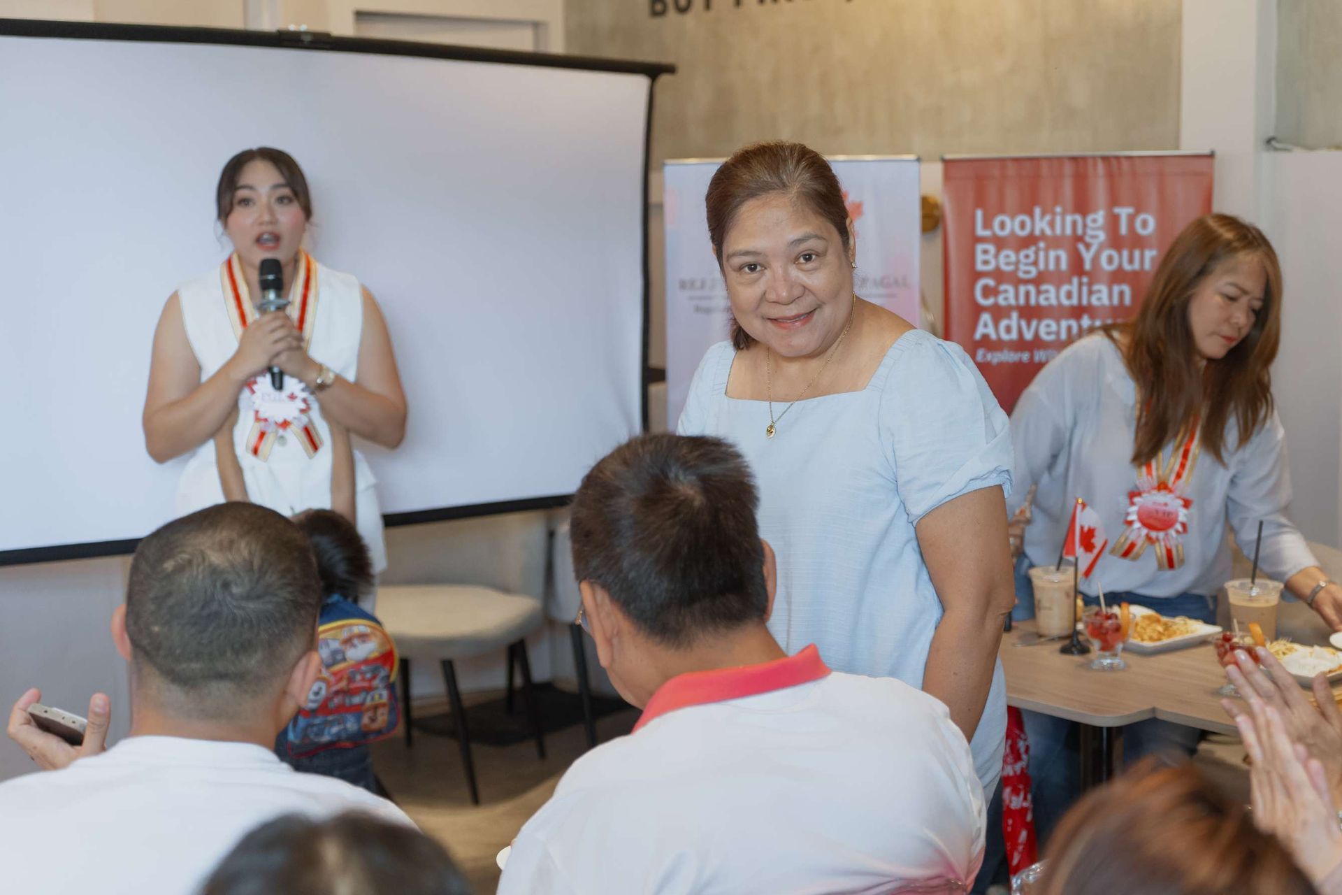 A woman is standing in front of a group of people holding a microphone.