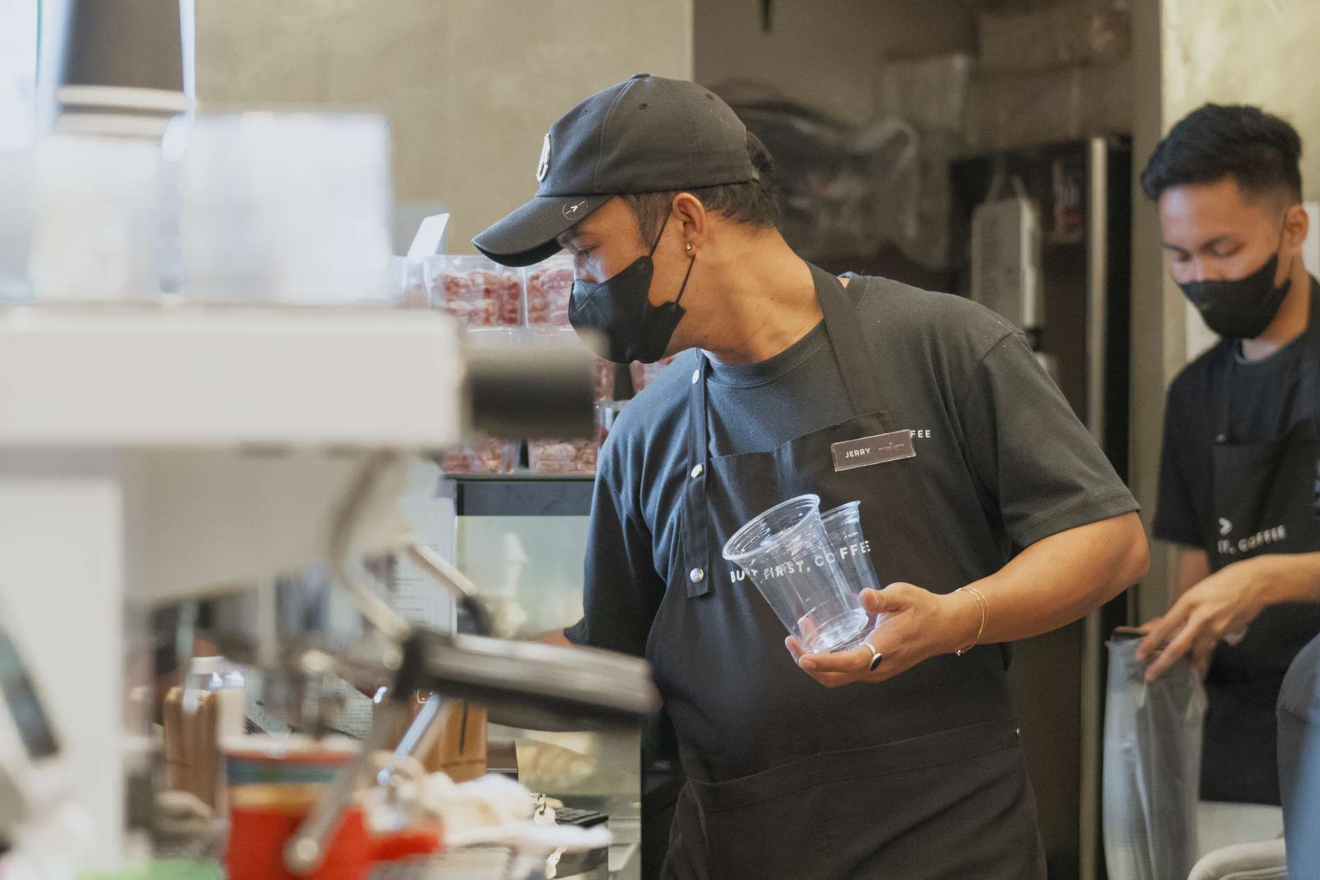 A man wearing a mask is holding a glass in a kitchen.