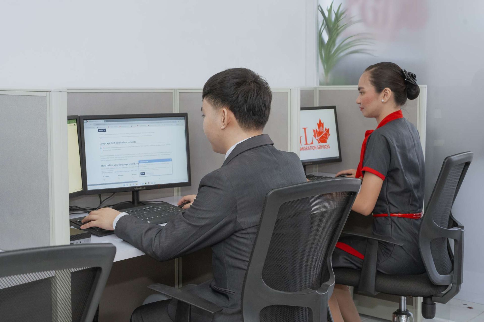 A man and a woman are sitting at a desk in front of a computer.