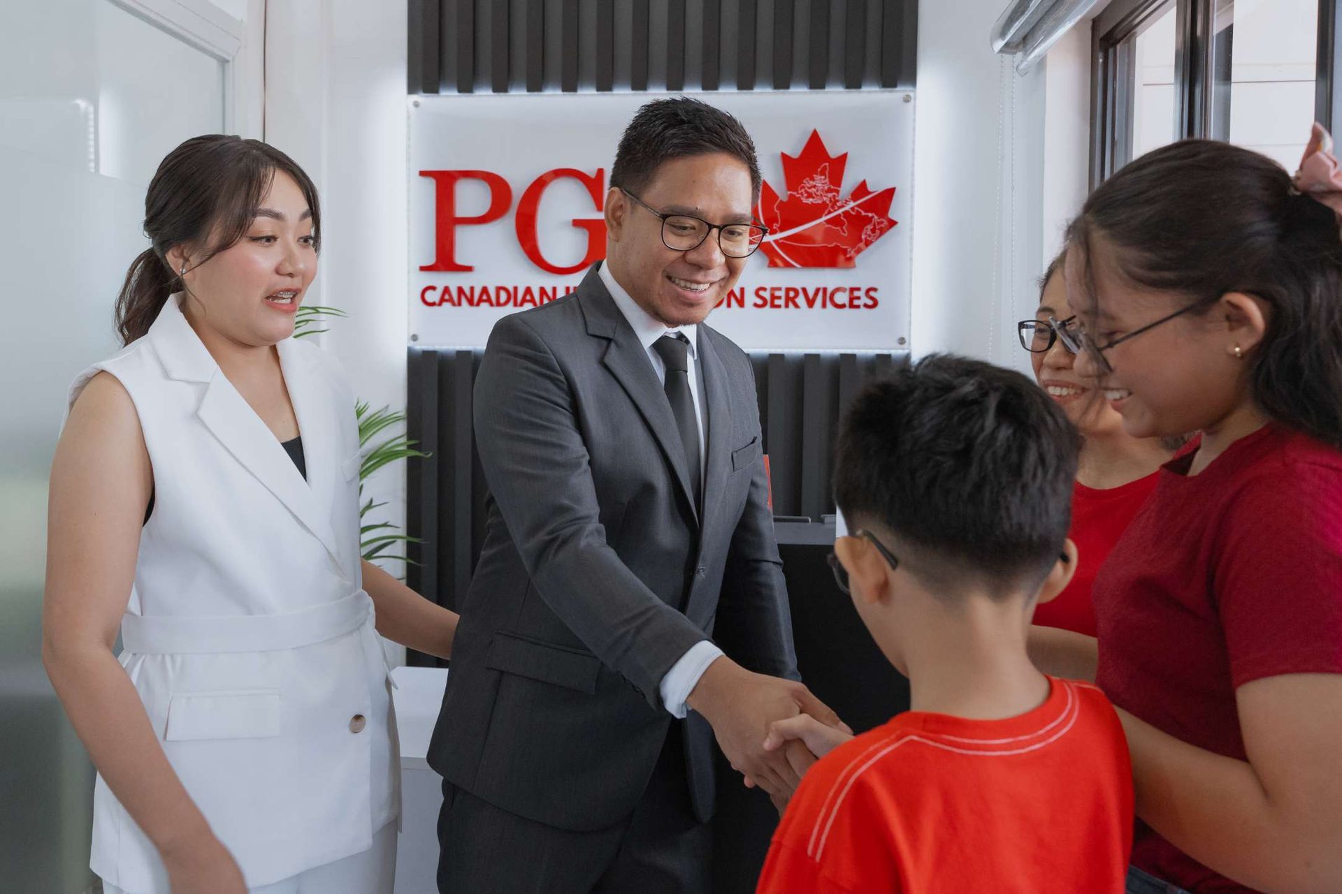 A man in a suit and tie is shaking hands with a boy in a red shirt.