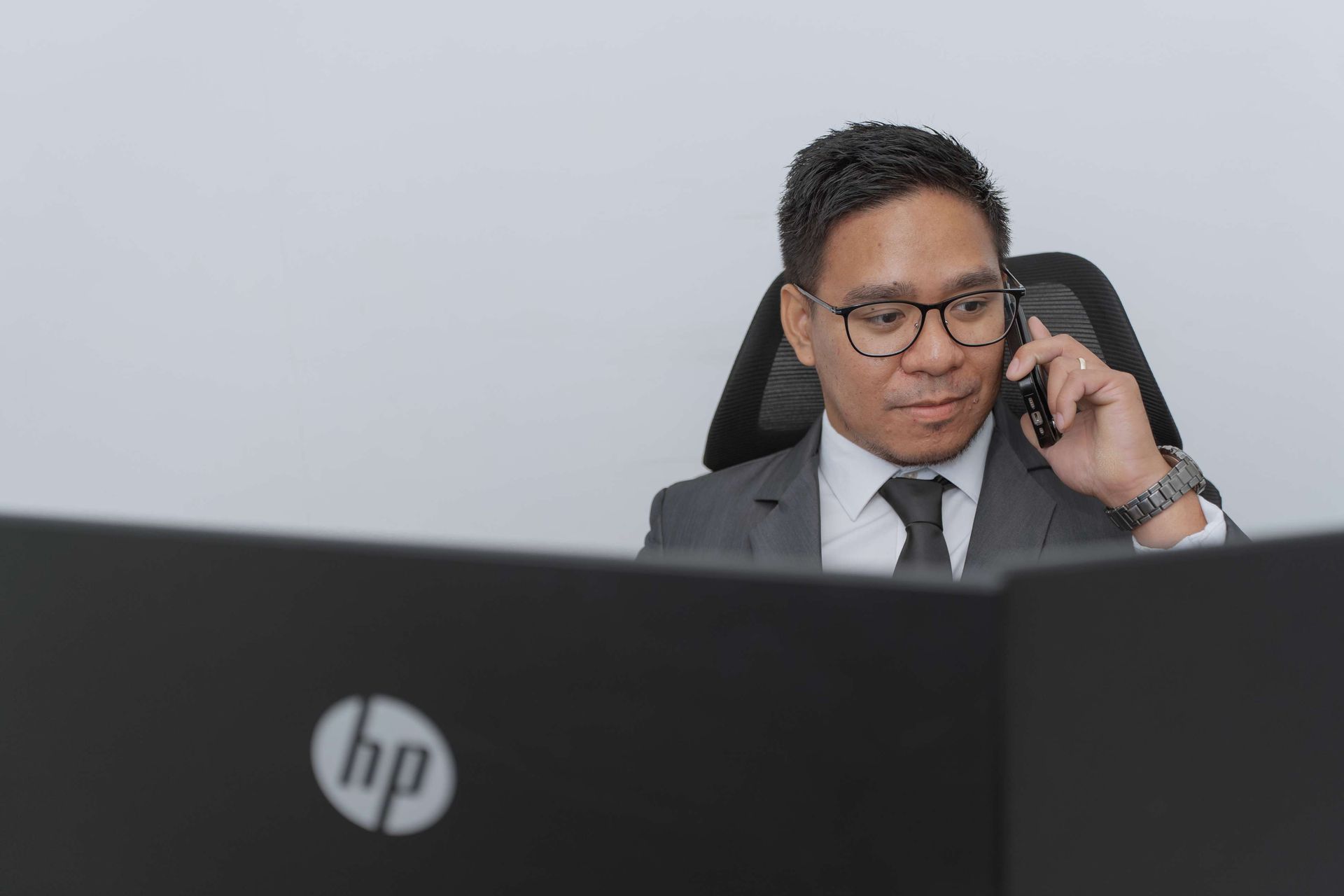 A man is sitting in front of a computer talking on a cell phone.