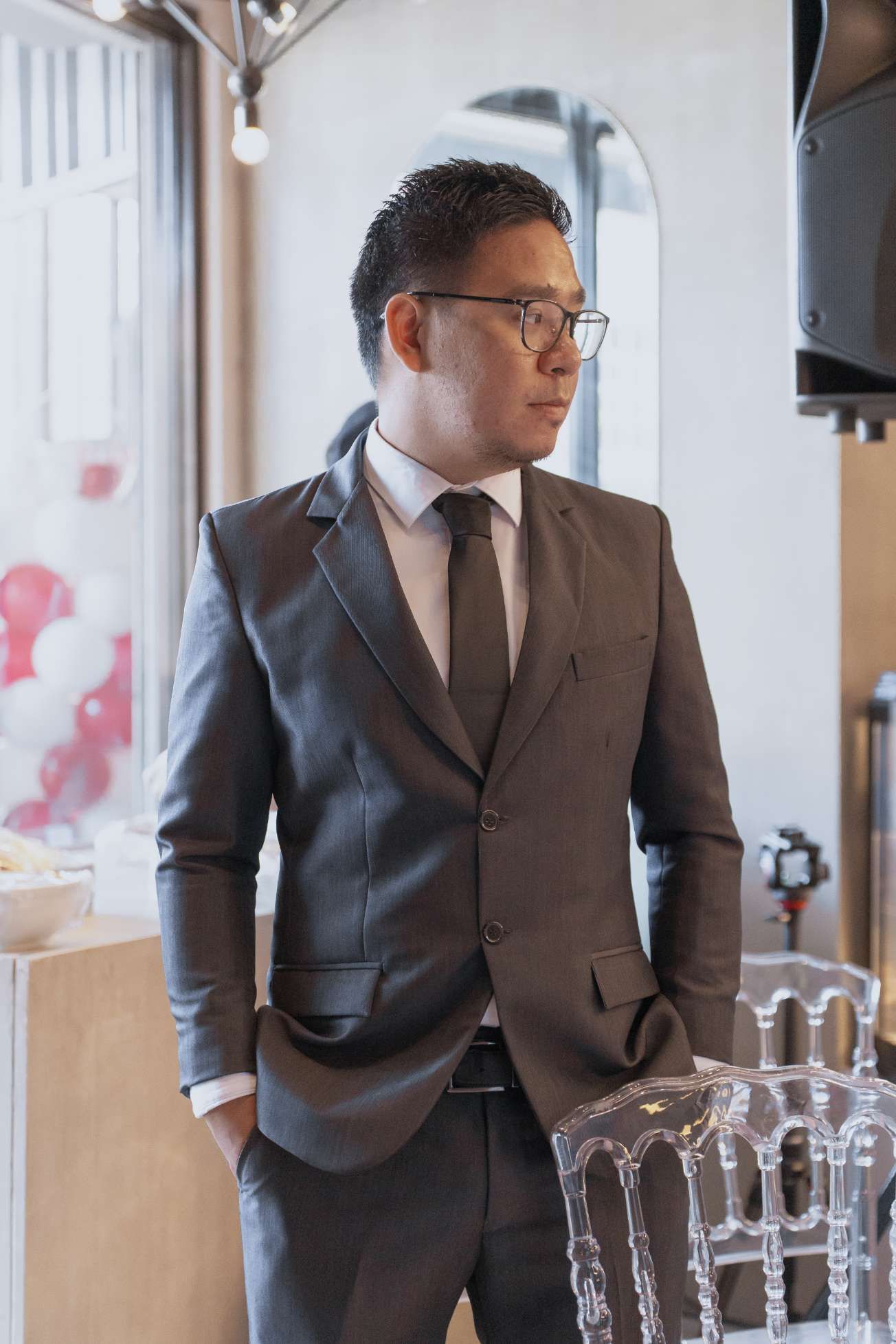 A man in a suit and tie is standing next to a clear chair.