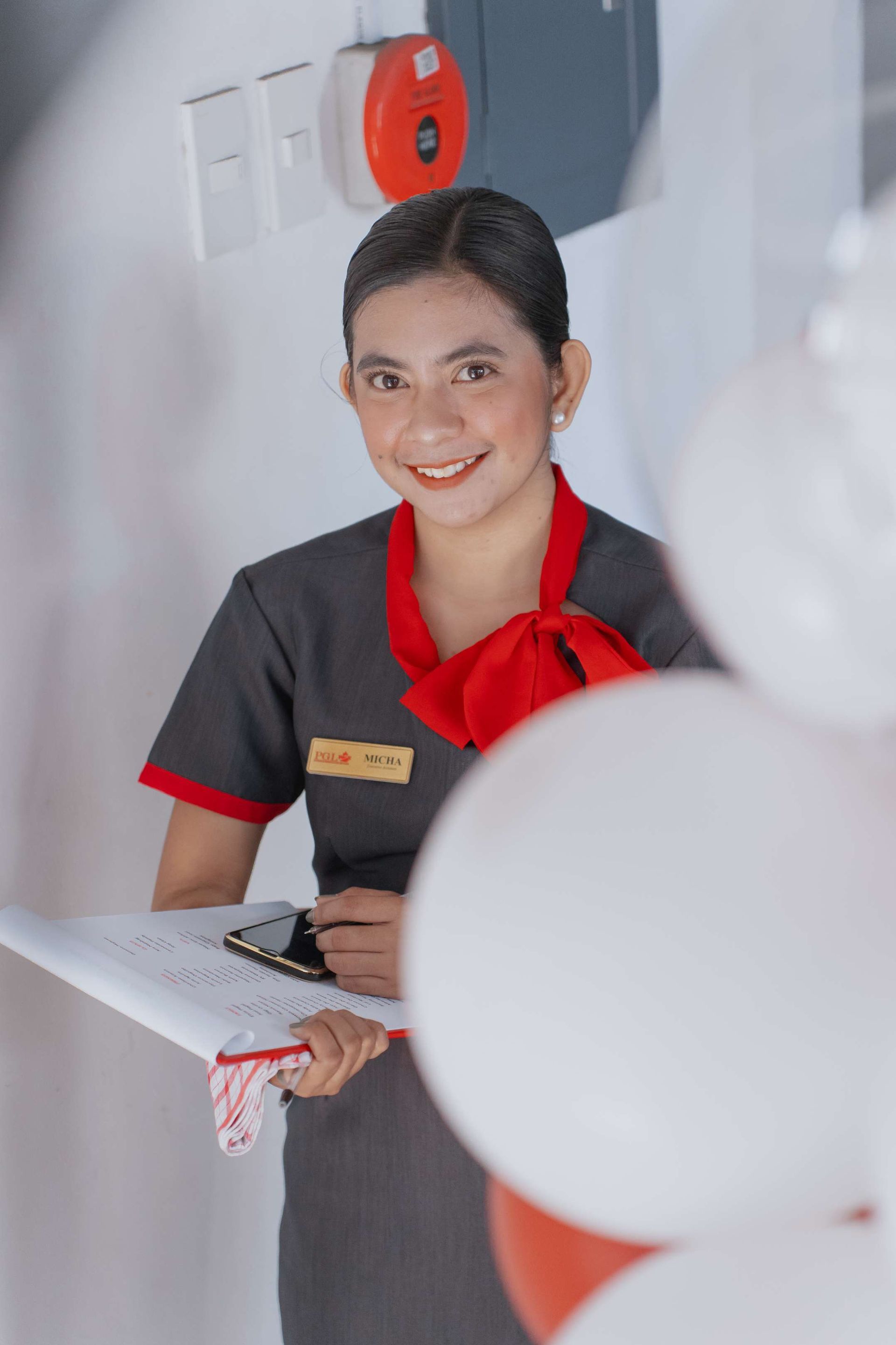 A woman is standing in front of balloons holding a clipboard and smiling.