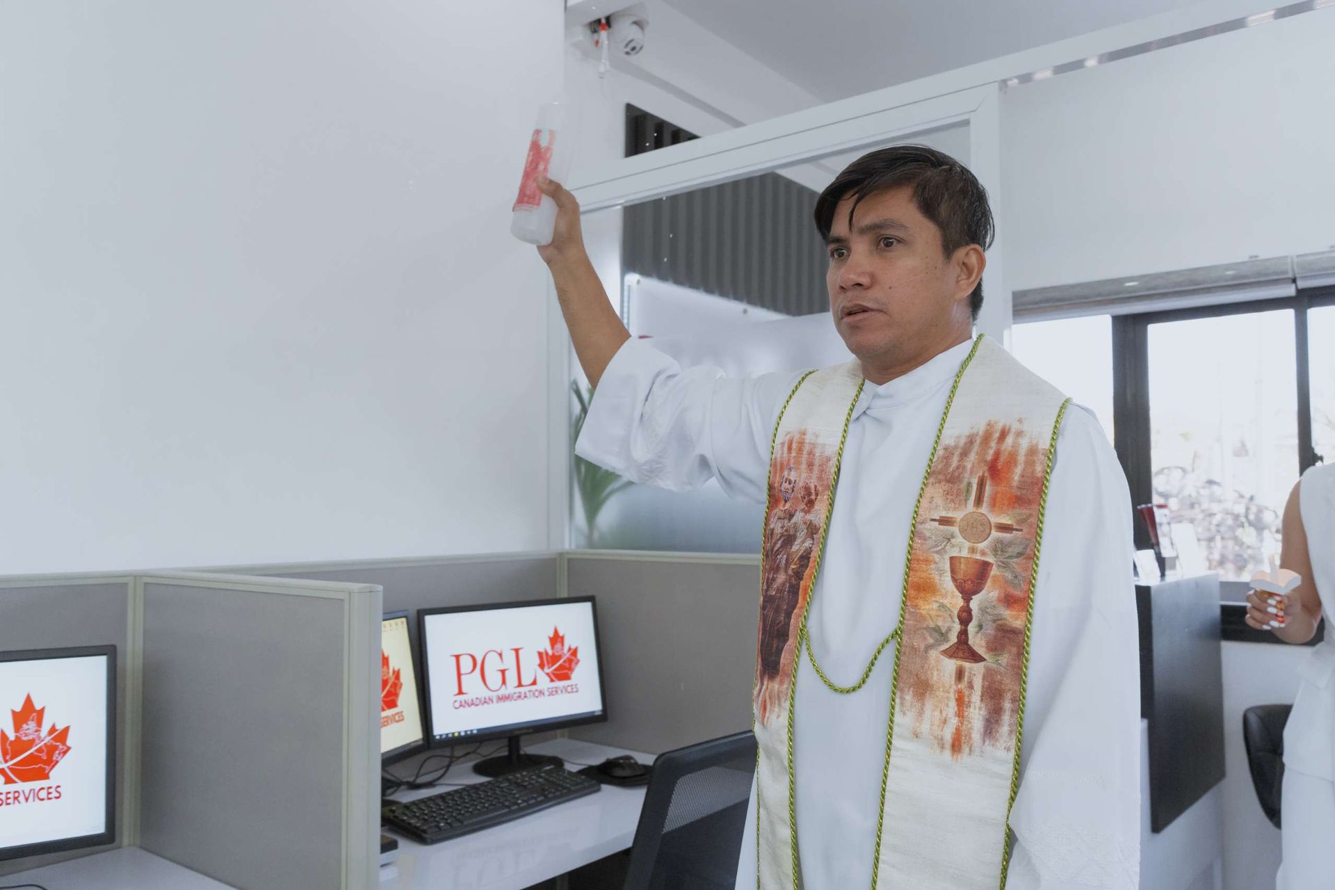 A man in a white robe is standing in front of a cubicle with a computer on it.